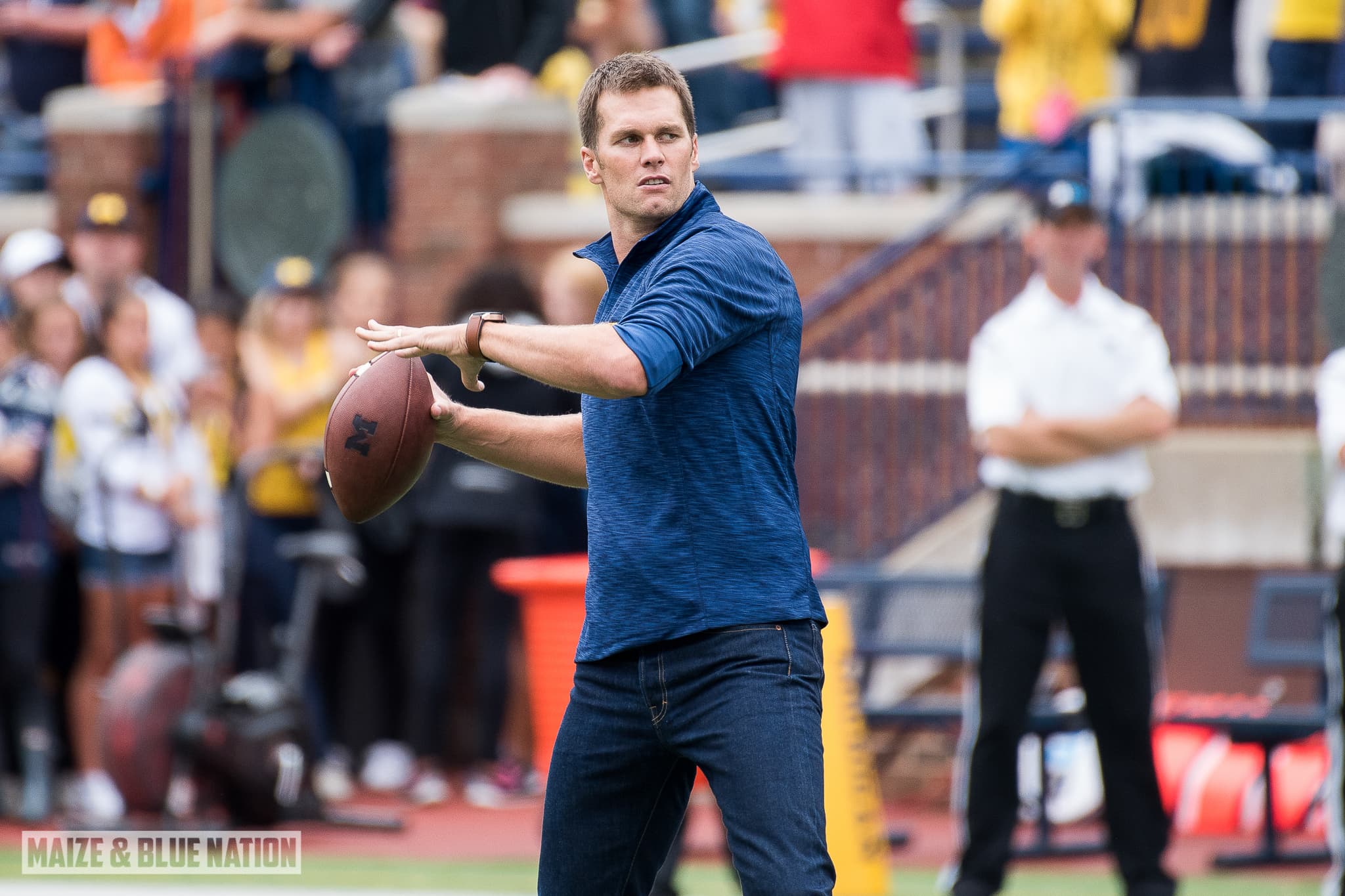 Tom Brady walking across a football field at Michigan Stadium in 2016.